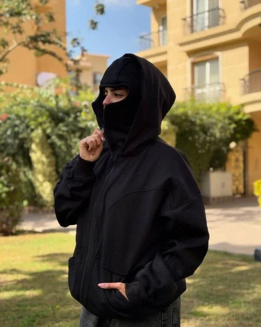 Unisex Ninja Balaclava Hoodie in black fleece with integrated face mask, worn outdoors for urban streetwear style and all-season comfort.