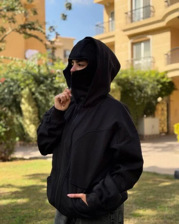 Unisex Ninja Balaclava Hoodie in black fleece with integrated face mask, worn outdoors for urban streetwear style and all-season comfort.