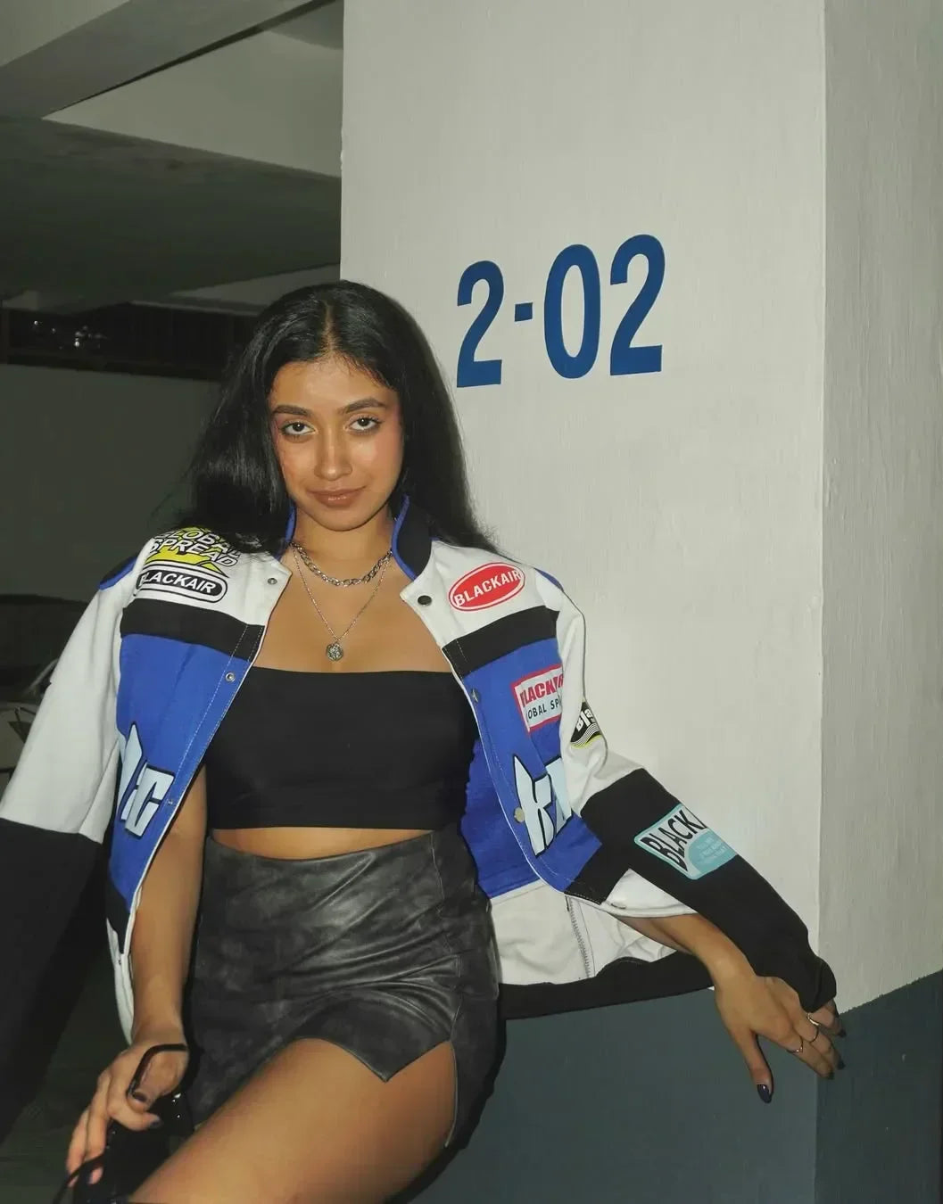 Blackair Racer Jacket - Vintage Style with retro motorsport patches in blue, white, and black, styled with a black crop top and leather skirt.