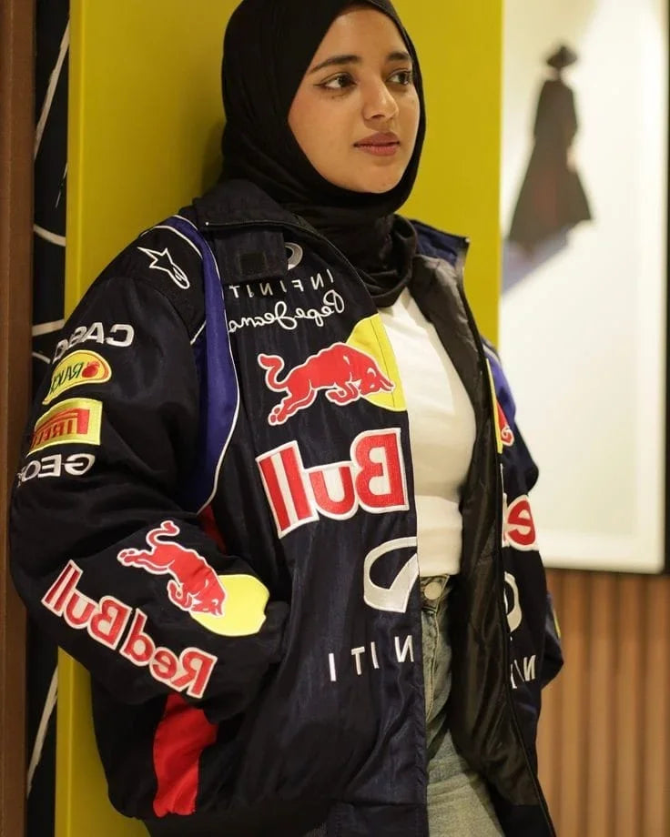 Woman in Red Bull Racing Jacket leaning against a wall. Blue jacket with bold logos, perfect for fans of racing and street style.