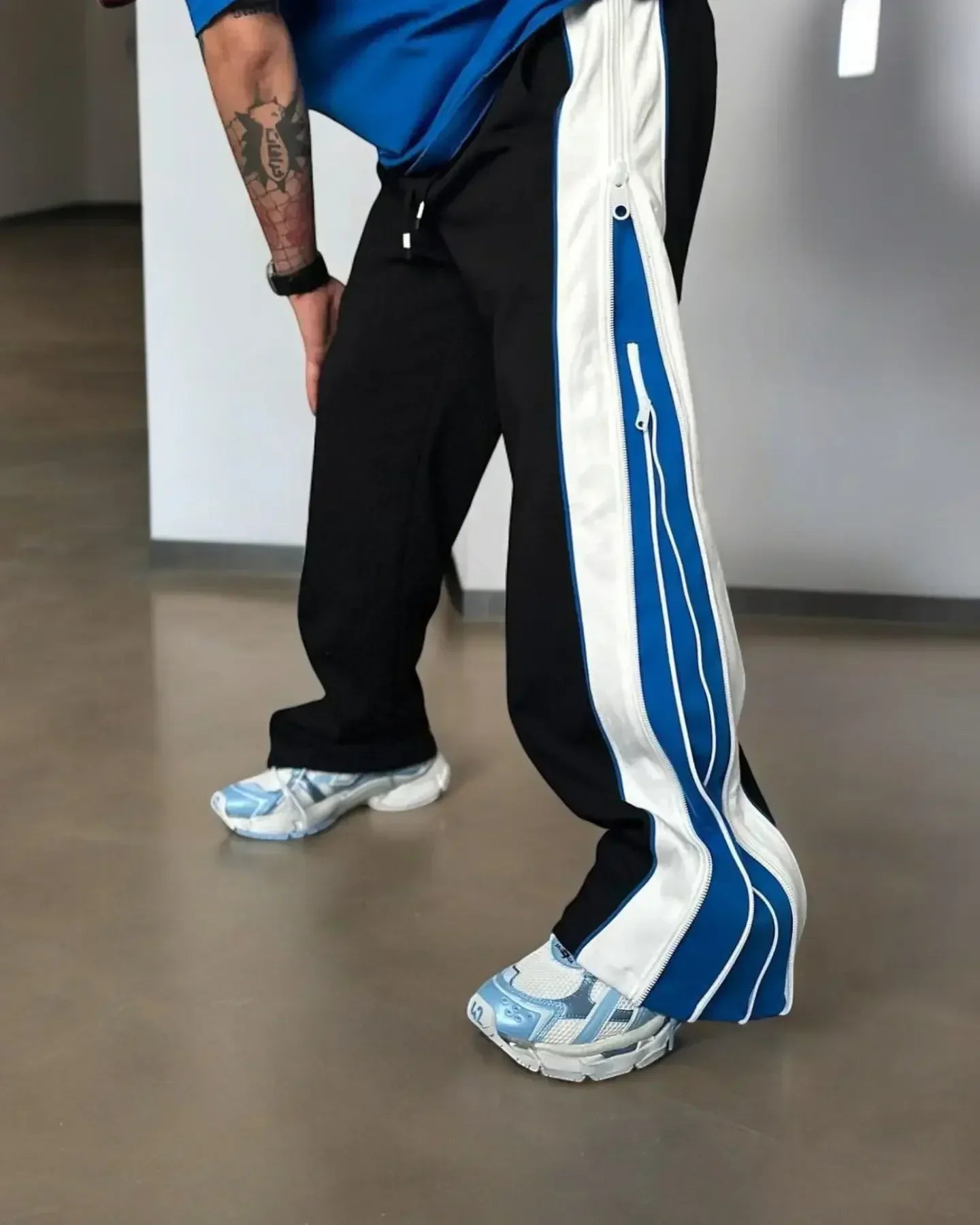 Shop Blue 3-Way Zip Baggy Pants Online featuring wide-leg black joggers with blue and white zip-up panels, styled with sneakers for urban flair.
